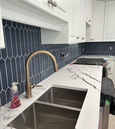 Image of a kitchen counter with navy blue honeycomb tiles, copper sink and white cabinets